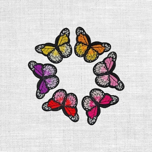 Könnte beinhalten: Gestickte Schmetterlingsaufnäher in kreisförmiger Anordnung. Jeder Schmetterling zeigt detaillierte Flügelmuster in leuchtenden Farben: Gelb, Orange, Rosa, Rot und Lila. Die Aufnäher sind schwarz umrandet und heben sich vom weißen Hintergrund ab.