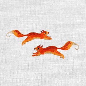 Könnte beinhalten: Zwei gestickte Eichhörnchen in Orange- und Rottönen sind auf einem weißen Stoffhintergrund in vollem Lauf dargestellt. Die Eichhörnchen haben detaillierte Merkmale, darunter kleine Ohren, dunkle Augen und flauschige Schwänze. Die Stickerei ist detailliert.