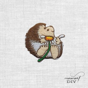 Könnte beinhalten: Gestickter Aufnäher mit einem Cartoon-Igel, der eine Gänseblümchen hält. Der Igel hat braunes und beiges Fell, ein hellbeige Gesicht und Füße. Das Gänseblümchen hat eine gelbe Mitte und weiße Blütenblätter. Der Aufnäher befindet sich auf weißem Hintergrund.