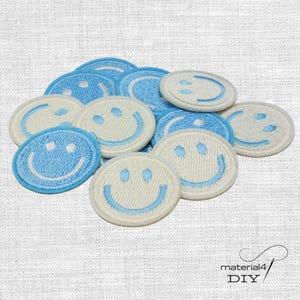Könnte beinhalten: Eine Ansammlung von aufgestickten Aufnähern mit einem Smiley-Gesicht-Design. Die runden Aufnäher haben einen weißen oder hellblauen Hintergrund und ein blaues Smiley-Gesicht. Geeignet für DIY-Projekte.