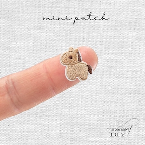 Könnte beinhalten: Ein kleiner, gestickter Aufnäher in Form eines Pferdes mit beigem Körper, brauner Mähne und Schweif sowie einem weißen Rand. Der Text "mini patch" steht über dem Aufnäher. Der Aufnäher wird von einem Finger gehalten.