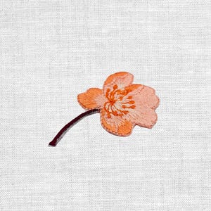 Könnte beinhalten: Gestickter Blumenaufnäher in Pfirsich- und Orangetönen mit einem dunkelbraunen Stiel. Die Blume hat detaillierte Stickereien, die ein strukturiertes Aussehen erzeugen. Der Aufnäher dient wahrscheinlich dekorativen Zwecken, z. B. zum Aufnähen auf Kleidung oder Accessoires.