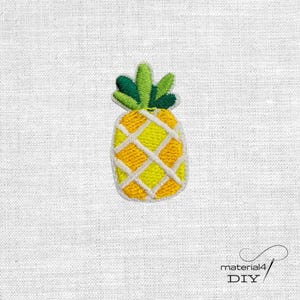 Könnte beinhalten: Ein gestickter Ananas-Aufnäher mit einem gelben Fruchtkörper, einem weißen gitterartigen Muster und grünen Blättern an der Oberseite. Das Design ist mit dichtem Garn gestickt und erzeugt eine strukturierte Optik auf weißem Stoff.