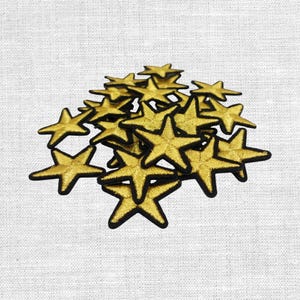 Könnte beinhalten: Eine Ansammlung goldener sternförmiger Aufnäher mit schwarzen Rändern. Die Aufnäher sind auf einem weißen Stoffhintergrund angeordnet. Die Sterne haben einen metallischen Glanz.
