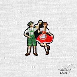 Könnte beinhalten: Ein gestickter Aufnäher mit zwei Figuren in traditioneller bayerischer Kleidung. Die linke Figur trägt eine grüne Hose und ein weißes Hemd, die rechte Figur einen roten Rock und eine weiße Bluse. Beide Figuren halten gelbe Bierkrüge in den Händen.