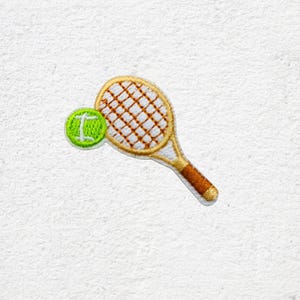 Könnte beinhalten: Gestickter Aufnäher mit einem Tennisschläger und Ball. Der Schläger hat einen beigen Rahmen, ein weißes Netz und einen braunen Griff. Der Tennisball ist grün mit einem weißen Streifen. Für Kleidung oder Accessoires.