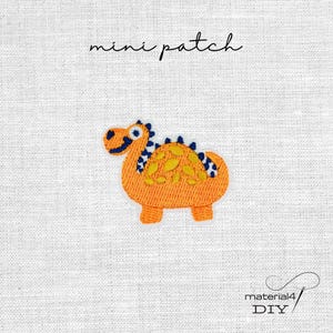 Könnte beinhalten: Gestickter orangefarbener Dinosaurier-Aufnäher mit blauen und gelben Akzenten. Der Aufnäher trägt den Schriftzug "mini patch" in Schreibschrift. Unten rechts steht der Text "material4 DIY".