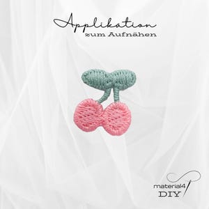 Könnte beinhalten: Gesticktes Kirsch-Patch mit rosa Kirschen und einem grünen Stiel und Blättern. Der Text "Applikation zum Aufnähen" ist oben in Schreibschrift geschrieben. In der unteren rechten Ecke steht "material4 DIY".