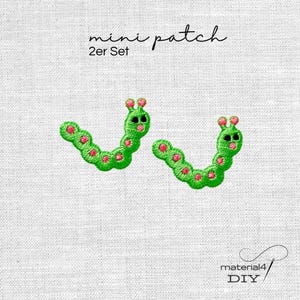 Könnte beinhalten: Ein Set aus zwei gestickten Mini-Aufnähern in Form von grünen Raupen mit rosa Punkten und schwarzen Augen. Der Text mini patch 2er Set steht oben, und der Text material4 DIY erscheint unten rechts im Bild.