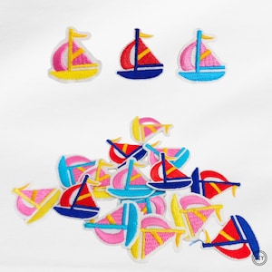 Könnte beinhalten: Eine Sammlung bunter, gestickter Segelboot-Patches. Jeder Patch hat eine weiße Umrandung, einen blauen Rumpf und Segel in Pink, Rot, Gelb und Blau. Die Patches eignen sich zum Dekorieren von Kleidung oder Accessoires.