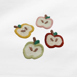 Könnte beinhalten: Vier gestickte Apfelaufnäher in Gelb, Rosa, Grün und Rot. Jeder Aufnäher ist als halber Apfel mit braunem Stiel und grünem Blatt gestaltet. Die Aufnäher befinden sich auf weißem Hintergrund.