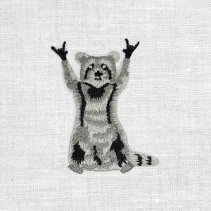 Könnte beinhalten: Gestickter Aufnäher mit einem Waschbären, der die Arme in einer Rock-and-Roll-Geste hebt. Der Waschbär ist in Grau- und Schwarztönen dargestellt, mit einem weißen Hintergrund. Der Aufnäher ist wahrscheinlich für Kleidung oder Accessoires gedacht.