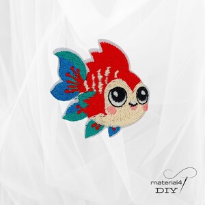 Könnte beinhalten: Gestickter Aufnäher eines Cartoon-Goldfischs mit großen, ausdrucksstarken Augen und einem lächelnden Mund. Der Fisch hat rote, blaue und türkisfarbene Details. Der Aufnäher befindet sich auf weißem Hintergrund. Der Text "material4 DIY" befindet sich unten rechts.