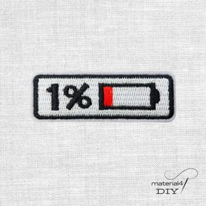 Könnte beinhalten: Gestickter Aufnäher mit schwarzem Rand, weißem Hintergrund und einem schwarzen Batteriesymbol, das 1 % Ladung anzeigt. Die Batterieanzeige hat eine rote Füllung, und der Text "1 %" ist in Schwarz dargestellt.