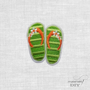 Könnte beinhalten: Gestickter Aufnäher mit einem Paar grüner Flip-Flops mit orangefarbenen Riemen und weißen und orangefarbenen Blumenakzenten. Die Flip-Flops haben ein gestreiftes Muster und sind weiß umrandet, auf weißem Stoff.