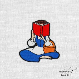 Könnte beinhalten: Gestickter Aufnäher mit einer Zeichentrickfigur, die ein Buch liest. Die Figur trägt ein blaues Kleid und eine weiße Schürze, mit einem roten Buch, das ihr Gesicht verdeckt. Ein orangefarbener Korb steht daneben. Der Aufnäher befindet sich auf einem weißen Stoffhintergrund.