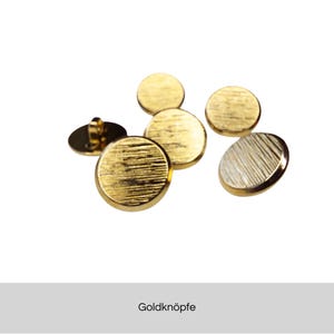 Könnte beinhalten: Eine Sammlung goldfarbener, runder Knöpfe mit einer strukturierten, geriffelten Oberfläche. Die Knöpfe sind verstreut, einer zeigt eine Schlaufe auf der Rückseite. Das Bild enthält den Text "Goldknöpfe".