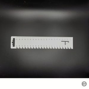 Könnte beinhalten: Ein silbernes Metalllineal mit gezackter Kante und Messmarkierungen. Das Lineal hat einen Griff mit Loch und ein kleines Logo. Das Lineal ist etwa 20 cm lang.