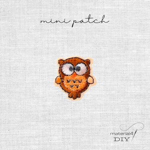 Könnte beinhalten: Ein kleiner, gestickter Eulenaufnäher in Braun- und Orangetönen mit großen weißen Augen. Der Text "mini patch" steht in Schreibschrift über der Eule. Der Aufnäher befindet sich auf einem weißen Stoffhintergrund.
