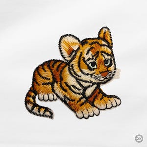 Könnte beinhalten: Gestickter Aufnäher eines Cartoon-Tigerbabys in Orange, Schwarz und Creme. Das Tigerbaby liegt mit traurigem Gesichtsausdruck. Der Aufnäher ist wahrscheinlich für DIY-Projekte gedacht.
