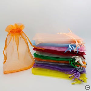Könnte beinhalten: Ein Stapel farbenfroher, durchsichtiger Organza-Geschenktüten in verschiedenen Farben, darunter Orange, Rosa, Blau, Rot, Grün, Lila und Gelb. Eine orangefarbene Tüte ist offen und zeigt den Kordelzug. Diese Tüten eignen sich für kleine Geschenke.
