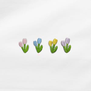 Könnte beinhalten: Vier gestickte Tulpenaufnäher in Rosa, Blau, Gelb und Lila. Jeder Aufnäher zeigt zwei oder drei Tulpen mit grünen Stielen und Blättern. Die Aufnäher sind für die Stoffverzierung bestimmt.