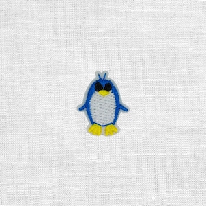 Könnte beinhalten: Ein gestickter Aufnäher mit einem stilisierten Pinguin, der einen blauen Körper, einen weißen Bauch, schwarze Augen und gelbe Füße hat. Das Design ist mit sichtbarer Textur gestickt und zeigt die detaillierte Naht der Vogelfigur.