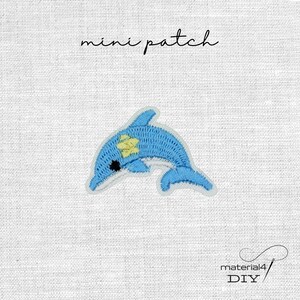 Könnte beinhalten: Ein Mini-Aufnäher mit einem gestickten blauen Delfin, der ein kleines gelbes Sterndetail auf dem Rücken hat. Der Delfin hat ein schwarzes Auge und ist in einer Sprungbewegung dargestellt. Der Text mini patch steht über dem Delfinmotiv.