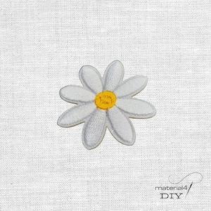 Könnte beinhalten: Gestickter Aufnäher mit einer Gänseblümchen-Blume mit weißen Blütenblättern und einem gelben Zentrum. Der Aufnäher befindet sich auf einem weißen Stoffhintergrund. Es ist ein DIY-Bastelartikel.