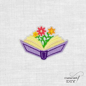 Könnte beinhalten: Gestickter Aufnäher mit einem offenen Buch mit gelben Seiten und einem lila Einband. Bunte Blumen in Rot, Gelb und Orange blühen aus dem Buch. Der Aufnäher hat einen weißen Rand und den Text "material4 DIY".