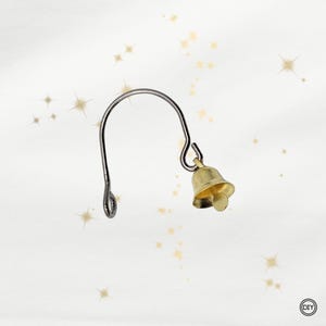 Könnte beinhalten: Ein kleiner, goldfarbener Glockenanhänger, der an einem silberfarbenen, gebogenen Ohrdraht befestigt ist. Die Glocke hat eine runde Form mit einem kleinen Klöppel. Der Ohrdraht hat unten eine Schlaufe zum Befestigen der Glocke.