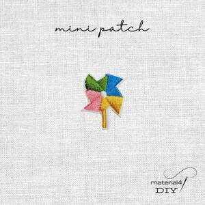 Könnte beinhalten: Ein gestickter Mini-Aufnäher mit einem bunten Windrad-Design aus grünen, blauen, gelben und rosafarbenen Segmenten auf einem gelben Stiel. Der Text "mini patch" steht über dem Motiv, "material4 DIY" steht in der unteren rechten Ecke.