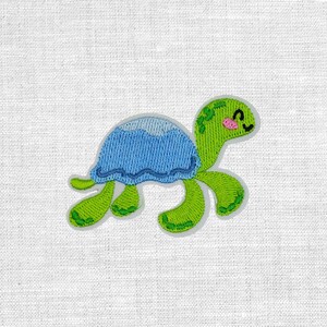 Könnte beinhalten: Ein gestickter Aufnäher, der eine grüne Schildkröte mit einem hellblauen Panzer zeigt. Die Schildkröte hat einen lächelnden Ausdruck mit einem kleinen rosa Wangendetail, dunklen Augen und einer strukturierten Stickerei am Körper und Panzer.