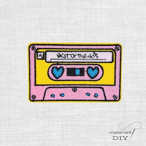 Könnte beinhalten: Gestickter Aufnäher in Form einer Musikkassette. Der Aufnäher ist rosa mit gelbem Mittelteil und trägt den Text "Best of the 80's". Zwei blaue Herzen sind auf dem Band. Der Aufnäher befindet sich auf weißem Hintergrund.
