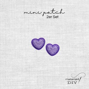 Könnte beinhalten: Ein Set aus zwei kleinen lila herzförmigen Stickaufnähern. Der Text "mini patch 2er Set" ist über den Herzen aufgedruckt, und der Text "material4 DIY" befindet sich in der unteren rechten Ecke des Bildes.
