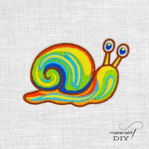Könnte beinhalten: Gestickter Schneckenaufnäher mit farbenfrohem Design. Das Schneckenhaus weist einen lebendigen Wirbel aus Gelb, Grün, Blau und Orange auf. Der Körper der Schnecke ist gelb mit blauen und grünen Akzenten. Der Aufnäher ist braun umrandet und auf einem weißen Stoff angebracht.