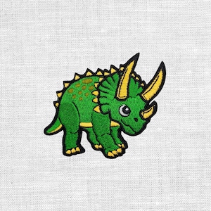 Könnte beinhalten: Gestickter Aufnäher mit einem grünen Triceratops-Dinosaurier mit gelben Hörnern und Akzenten. Der Aufnäher hat ein detailliertes Design und eignet sich für Kleidung oder Accessoires.