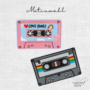 Könnte beinhalten: Zwei gestickte Aufnäher mit Kassetten-Motiven. Ein Aufnäher ist rosa und hellblau mit einem roten Herz, einem Regenbogen und dem Text LOVE SONGS. Der zweite Aufnäher ist grau mit einem Regenbogenstreifen und dem Text 90 und SIDE B.