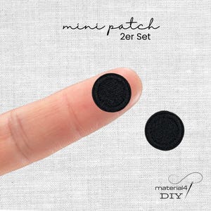 Könnte beinhalten: Ein Set aus zwei kleinen, runden, schwarzen Stickaufnähern. Der Text "mini patch 2er Set" ist oben und der Text "material4 DIY" ist unten zu sehen. Die Aufnäher haben eine texturierte, gestickte Oberfläche.