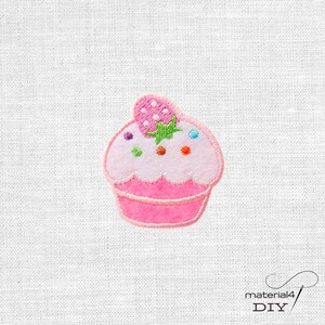 Könnte beinhalten: Ein gestickter Aufnäher in Form eines Cupcakes mit rosa Basis, hellrosa Zuckerguss und einer Erdbeere obenauf. Das Design zeigt kleine bunte Punkte als Streusel und den Text material4 DIY in der unteren rechten Ecke.