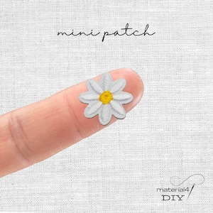 Könnte beinhalten: Ein kleiner gestickter Gänseblümchen-Aufnäher mit weißen Blütenblättern und einem gelben Zentrum. Der Text 'mini patch' steht über der Blume und der Text 'material4 DIY' befindet sich in der unteren rechten Ecke auf weißem Texturgrund.