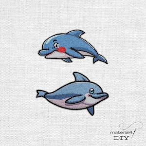 Könnte beinhalten: Zwei gestickte Aufbügler in Form von Cartoon-Delfinen in Blau-, Weiß- und Rosatönen. Der obere Delfin hat einen roten Wangenfleck, der untere einen hellrosa Bauch. Beide Aufnäher sind mit schwarzen Konturen und Stickereien versehen.