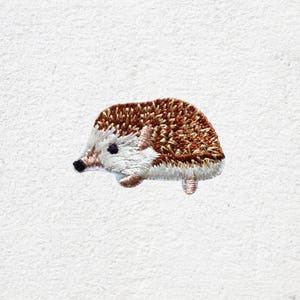 May include: Embroidered patch of a hedgehog. The patch features a brown and white hedgehog with a black nose and small, detailed legs. The hedgehog is set against a white background.