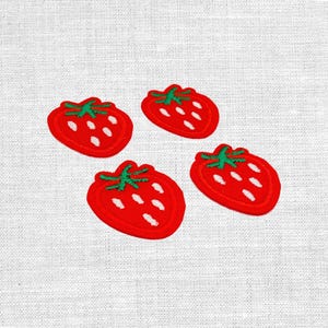 Könnte beinhalten: Vier gestickte Erdbeer-Patches. Jeder Patch zeigt eine leuchtend rote Erdbeere mit grünem Stiel und weißen Samen. Die Patches sind auf einem weißen Stoffhintergrund angeordnet.
