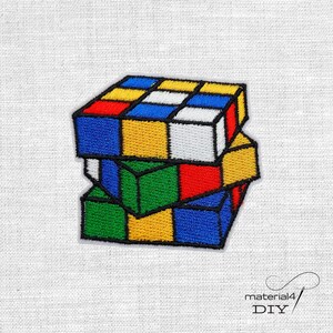 Könnte beinhalten: Gestickter Aufnäher mit einem bunten Rubik's Cube-Design. Der Würfel besteht aus Quadraten in Rot, Blau, Gelb, Grün und Weiß, umrandet in Schwarz. Der Aufnäher befindet sich auf einem weißen Stoffhintergrund. Der Text "material4 DIY" befindet sich unten rechts.