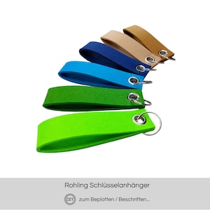 Könnte beinhalten: Eine Auswahl an Filz-Schlüsselanhängern in verschiedenen Farben, darunter Grün, Blau, Beige und Braun, jeweils mit einem silbernen Metallring. Die Schlüsselanhänger sind auf weißem Hintergrund fächerförmig angeordnet. Der Text lautet "Rohling Schlüsselanhänger".