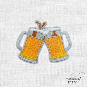 Könnte beinhalten: Ein gestickter Aufnäher mit zwei aneinanderstoßenden Bierkrügen. Die Krüge sind mit goldgelber Flüssigkeit gefüllt, mit weißem Schaum bedeckt und haben graue Henkel sowie Umrandungen. Das Design zeigt orangefarbene Spritzer über dem Schaum.