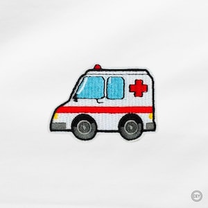 Könnte beinhalten: Gestickter Aufnäher eines weißen Krankenwagens mit rotem Streifen und Kreuz. Der Krankenwagen hat blaue Fenster, schwarze Räder und ein rotes Licht oben. Ein lustiger, dekorativer Aufnäher für Kleidung oder Accessoires.