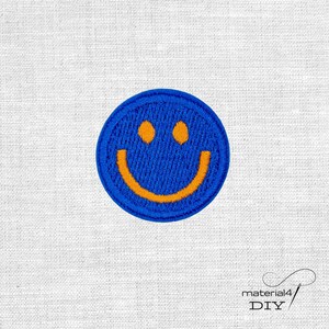 Könnte beinhalten: Ein kreisförmiger gestickter Aufnäher mit blauem Hintergrund und einem leuchtend orangefarbenen Smiley-Gesicht. Der Aufnäher hat einen gestickten Rand und zeigt einen einfachen, klassischen fröhlichen Ausdruck mit zwei runden Augen und einem geschwungenen Mund.
