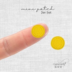 Könnte beinhalten: Ein Set aus zwei kleinen, runden, gelben Stickaufnähern. Der Text "mini patch 2er Set" ist oben aufgedruckt, und der Text "material4 DIY" befindet sich unten. Die Aufnäher weisen ein dichtes, strukturiertes Fadenmuster auf.
